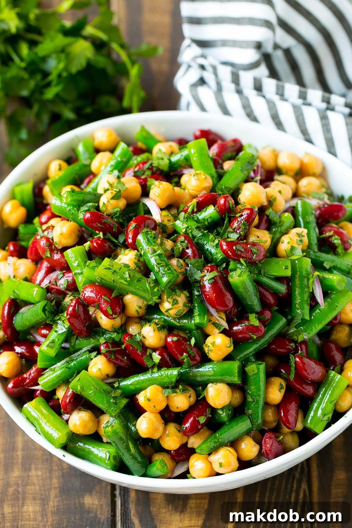 A bowl filled with three different types of beans (kidney, garbanzo, green) generously topped with dressing and fresh parsley, ready to be served.