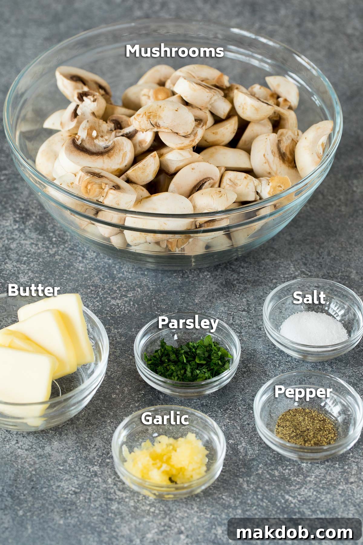 Bowls of fresh ingredients for sauteed mushrooms, including whole button mushrooms, a stick of butter, minced garlic, and fresh parsley, all ready for preparation.