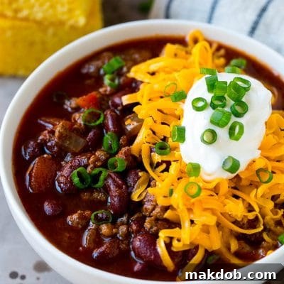 A bowl of slow cooker chili topped with shredded cheese, sour cream and green onions.