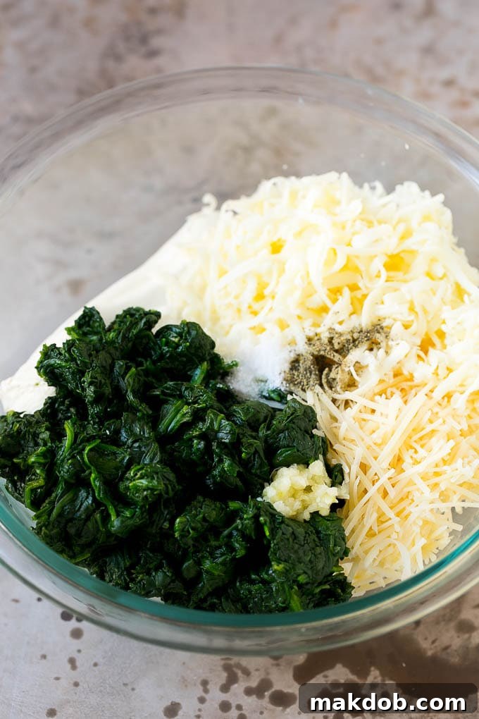 Ingredients for hot spinach dip: cooked spinach, garlic, shredded cheese, cream cheese, and sour cream in a mixing bowl.
