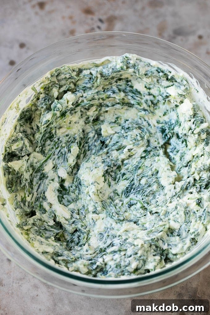 Creamy mixture of spinach, cheeses, and sour cream stirred together for hot spinach dip.