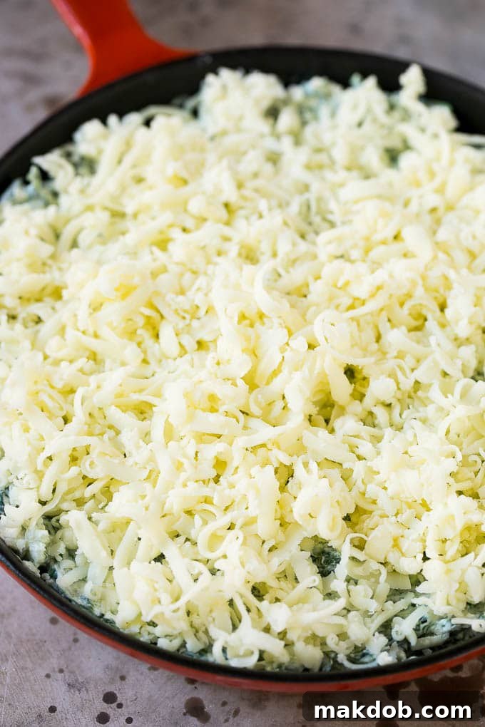 An unbaked skillet of spinach dip topped with a generous layer of shredded mozzarella cheese, ready for the oven.