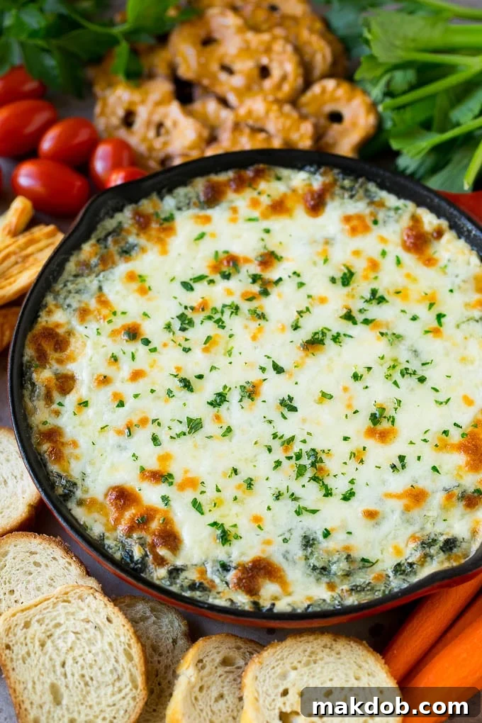 A golden-brown skillet of hot spinach dip, garnished with fresh parsley and served with an assortment of crackers, bread, and vegetable sticks.