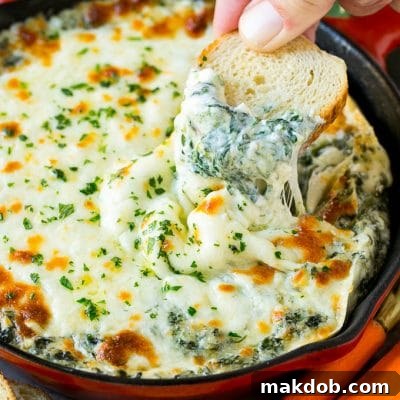 A piece of bread scooping into a bubbling hot spinach dip.