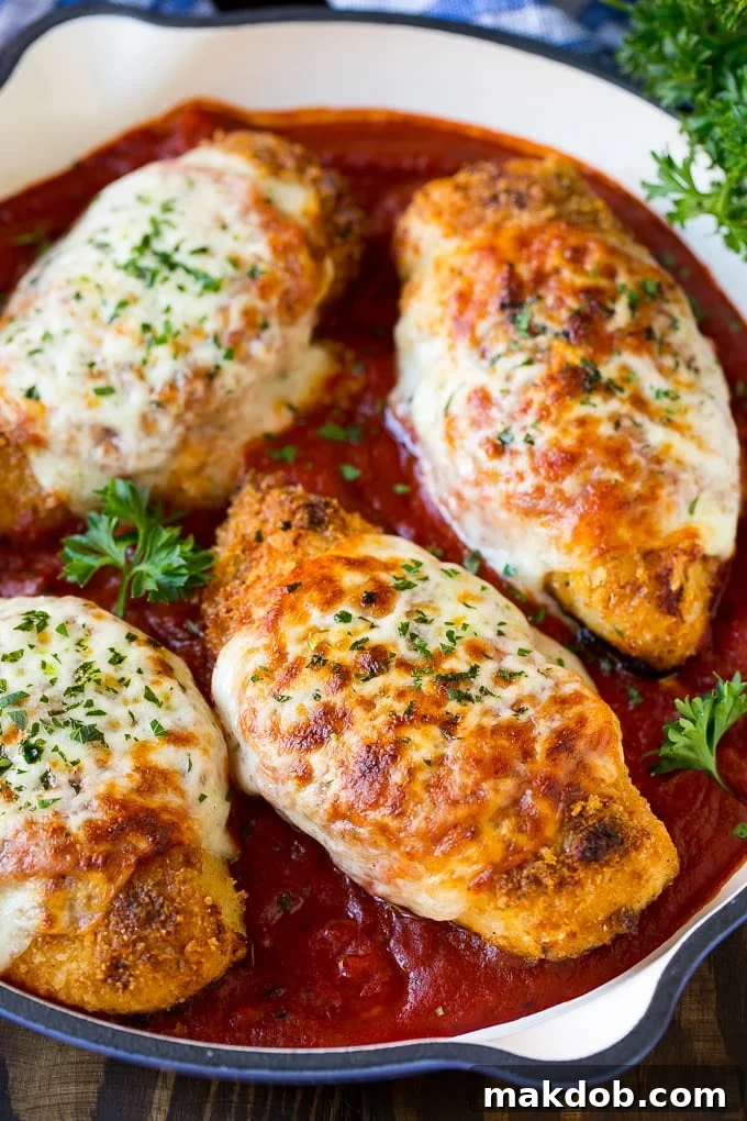 A skillet of baked chicken parmesan with crispy chicken breasts, marinara sauce and melted cheese.