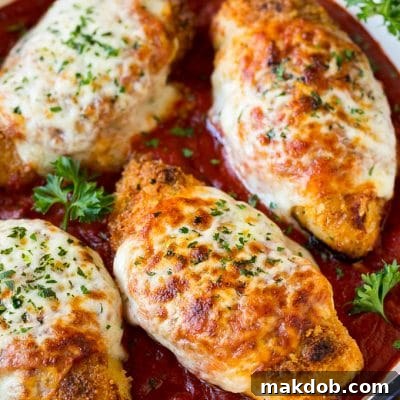 A skillet of baked chicken parmesan with crispy chicken breasts, marinara sauce and melted cheese.