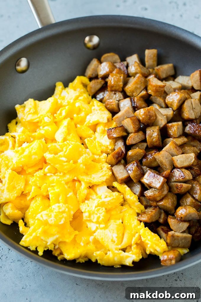 Diced sausage and fluffy scrambled eggs cooking in a pan.