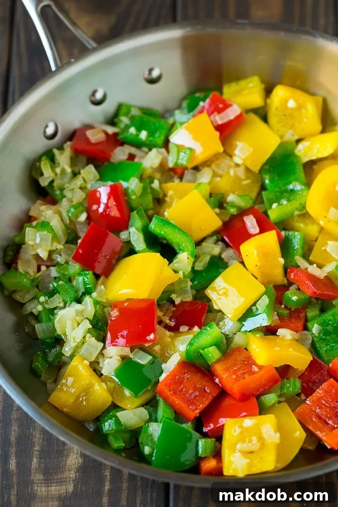 Diced bell peppers, onion, and minced garlic being sautéed in a large skillet, forming the flavorful base for jambalaya.