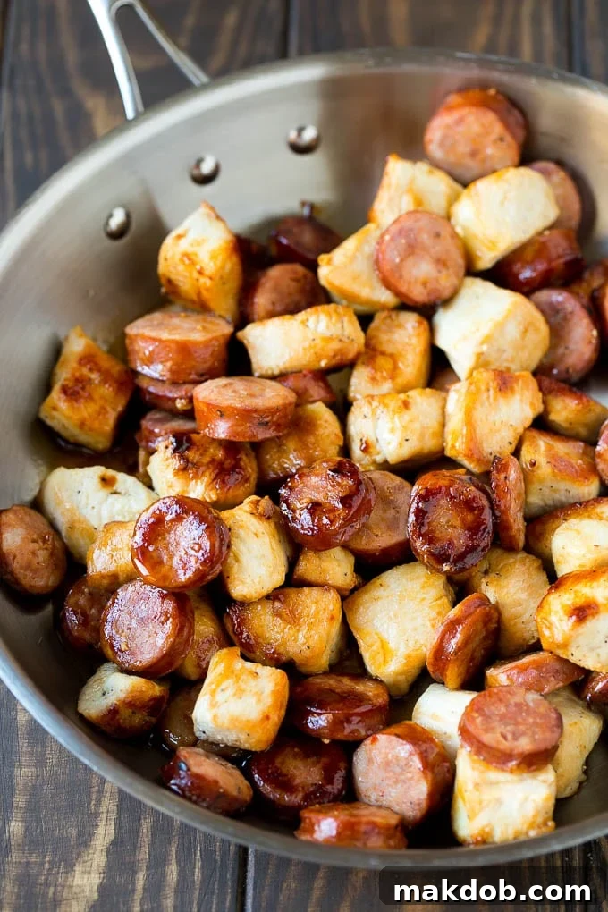 A large pan filled with sautéed chicken pieces and perfectly browned andouille sausage, prepared for the next step of jambalaya.