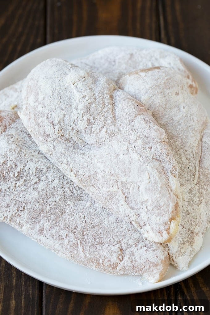 Raw chicken breasts coated in a seasoned flour mixture, ready for cooking.