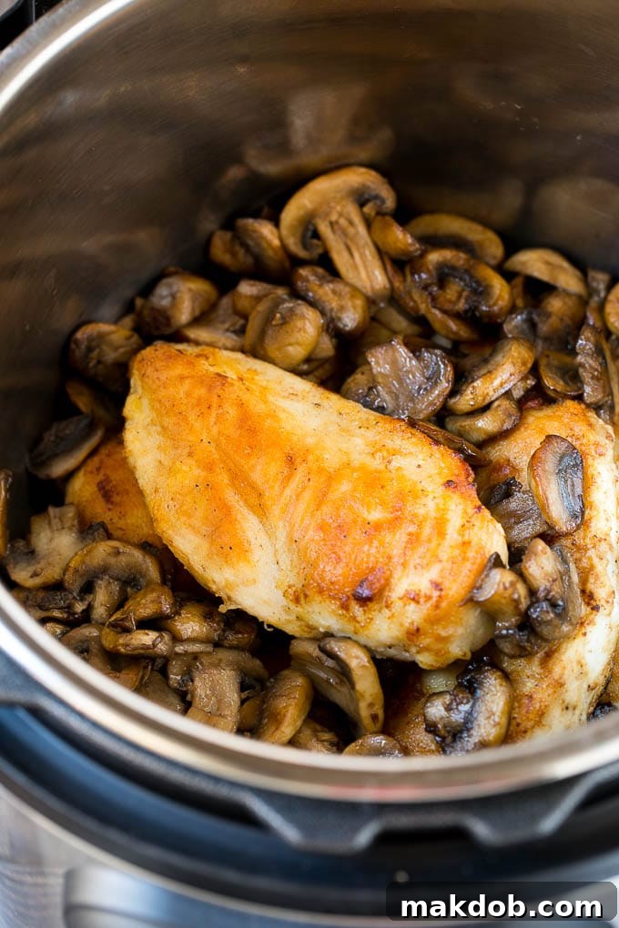 Chicken breasts and sauteed mushrooms nestled together in an Instant Pot, ready for pressure cooking.