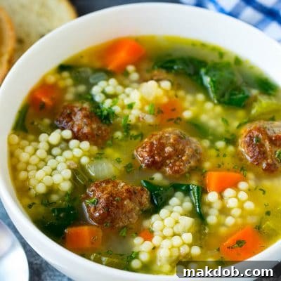 A bowl of Italian wedding soup with meatballs, carrots, spinach and pasta.