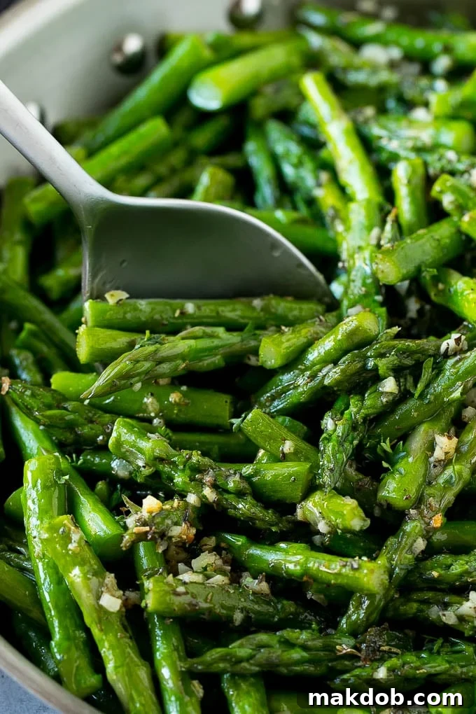 A serving spoon in a pan of garlic and herb sauteed asparagus.