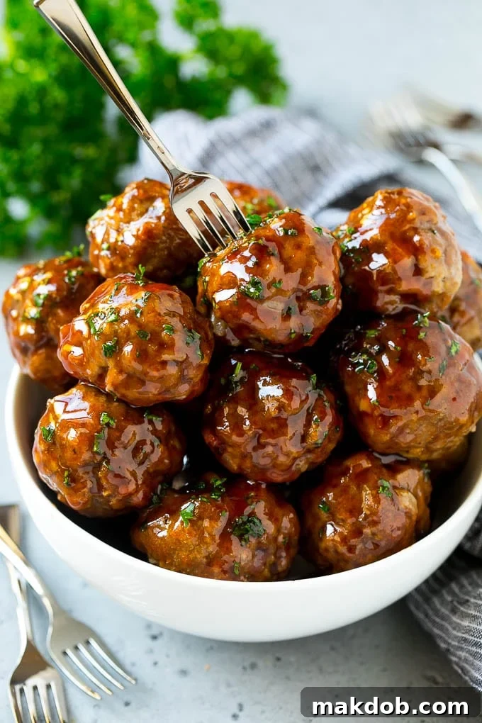 Sweet and Sour Meatballs Recipe | Slow Cooker Meatballs | Crockpot Meatballs | Cocktail Meatballs #meatballs #beef #slowcooker #crockpot #dinner #appetizer #dinneratthezoo A bowl of sweet and sour meatballs with a cocktail fork in it.