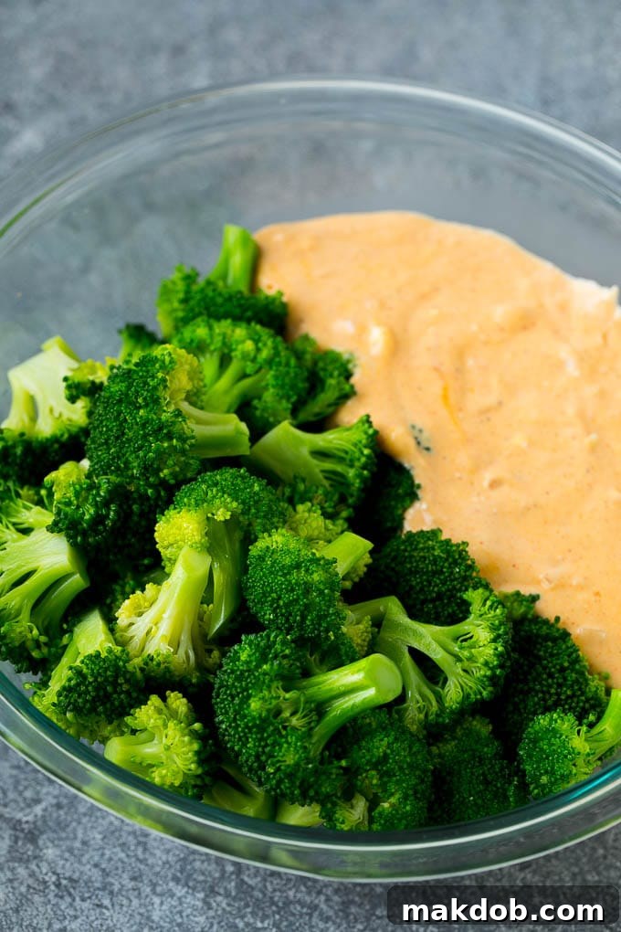 Cooked broccoli florets mingling with a rich, melted cheese sauce in a mixing bowl, ready to be transferred to a baking dish.