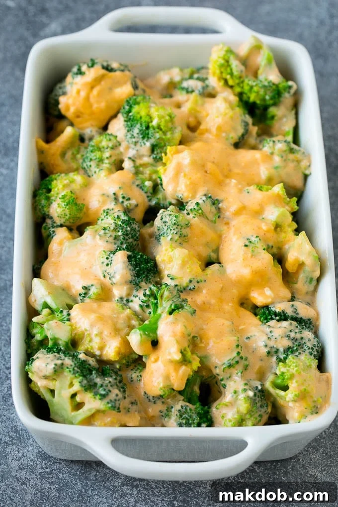 Broccoli florets generously coated in a creamy cheese sauce, nestled in a baking dish, and topped with shredded cheese, ready for the oven.