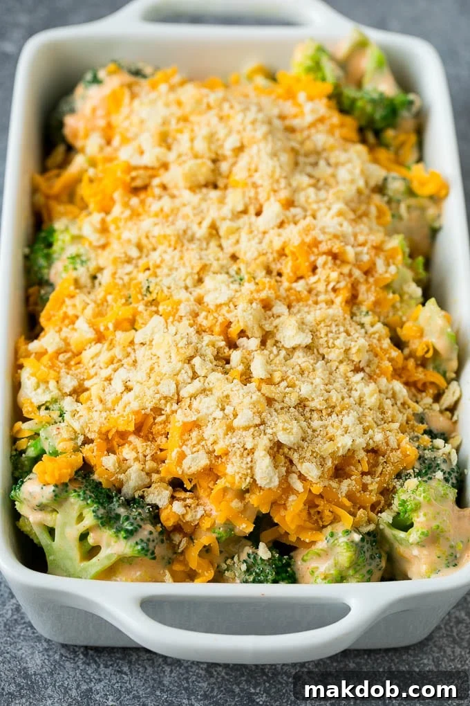 Broccoli in cheese sauce, generously topped with crushed crackers and shredded cheese, showcasing the texture before baking.