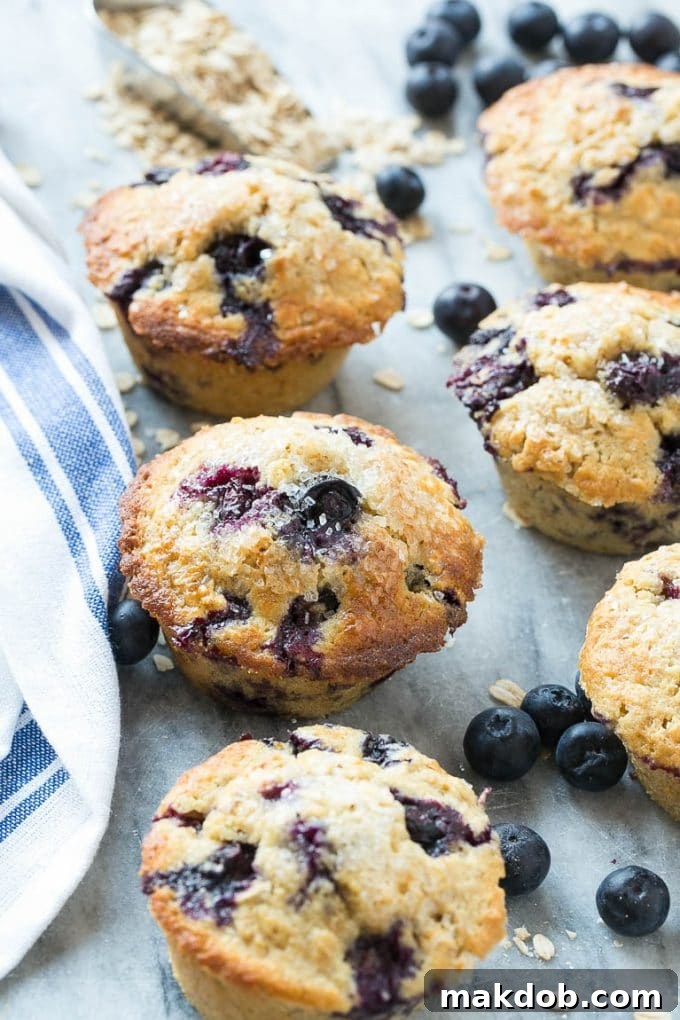 Multiple healthy blueberry muffins on a marble slab with fresh blueberries.