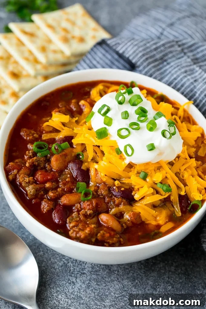 A bowl of Instant Pot chili topped with sour cream, cheese and green onions, ready to be served.