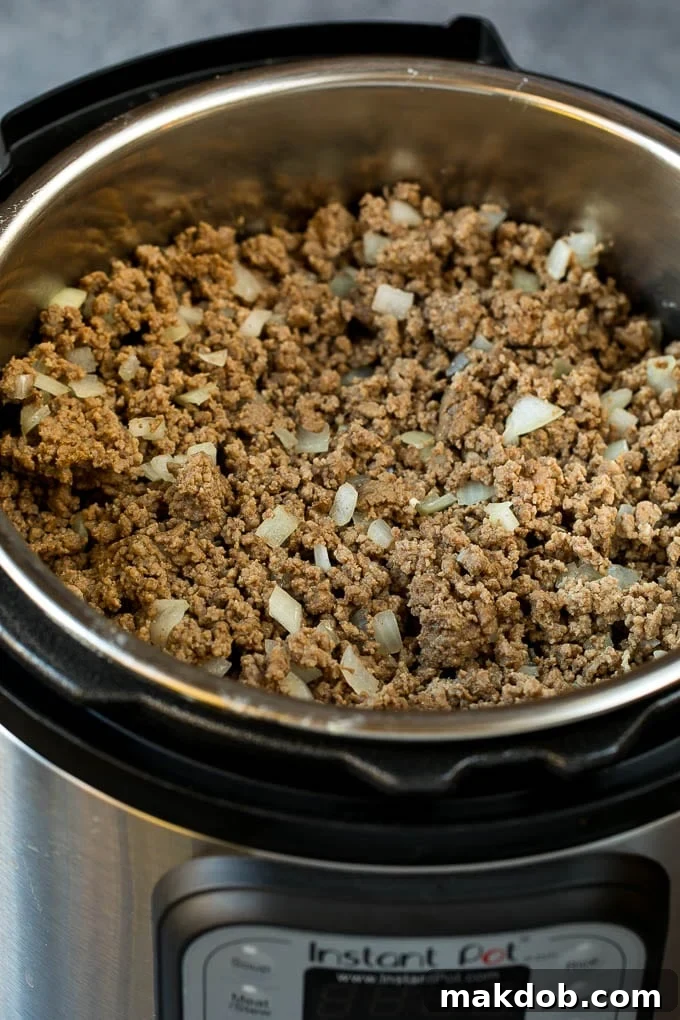 Ground beef and onions browning in an Instant Pot.
