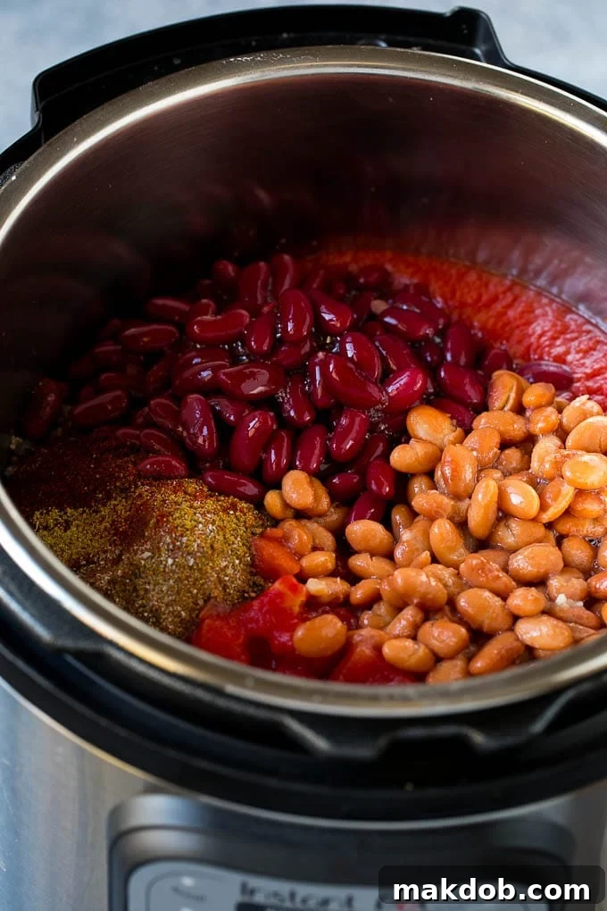 Pinto beans, kidney beans, spices and tomatoes layered in an Instant Pot before cooking.