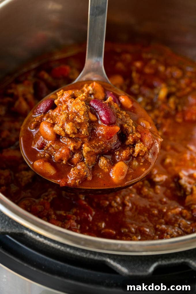 A ladle full of Instant Pot chili with chunks of beef and beans.