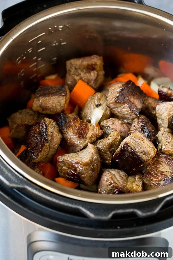 Beef stew meat and various vegetables browning inside an Instant Pot, showing the initial stages of flavor development.