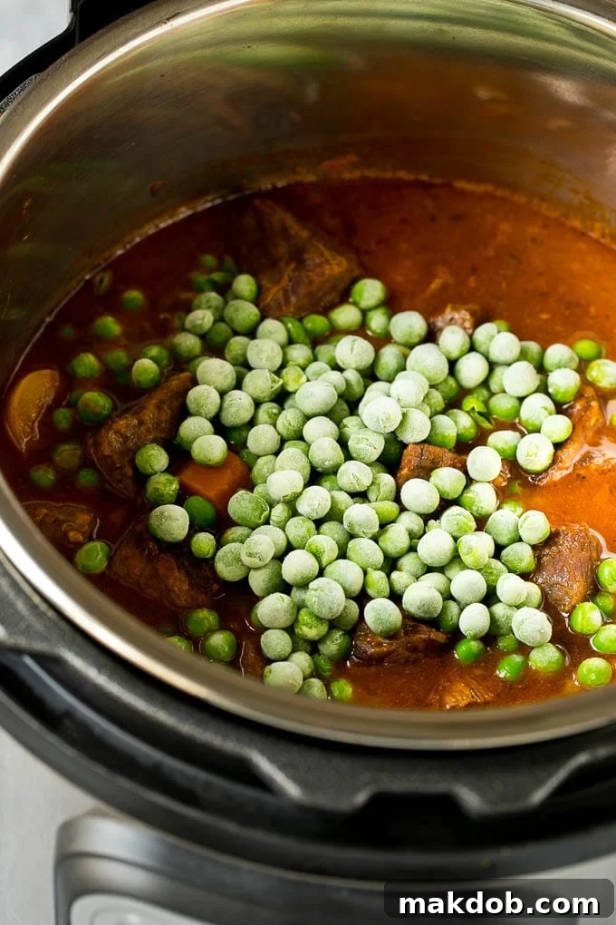 A close-up shot of vibrant green frozen peas being added to a simmering Instant Pot beef stew, enhancing color and freshness.