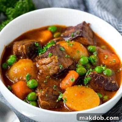 A bowl of Instant Pot beef stew with cubes of meat, potatoes, carrots, onions and peas.