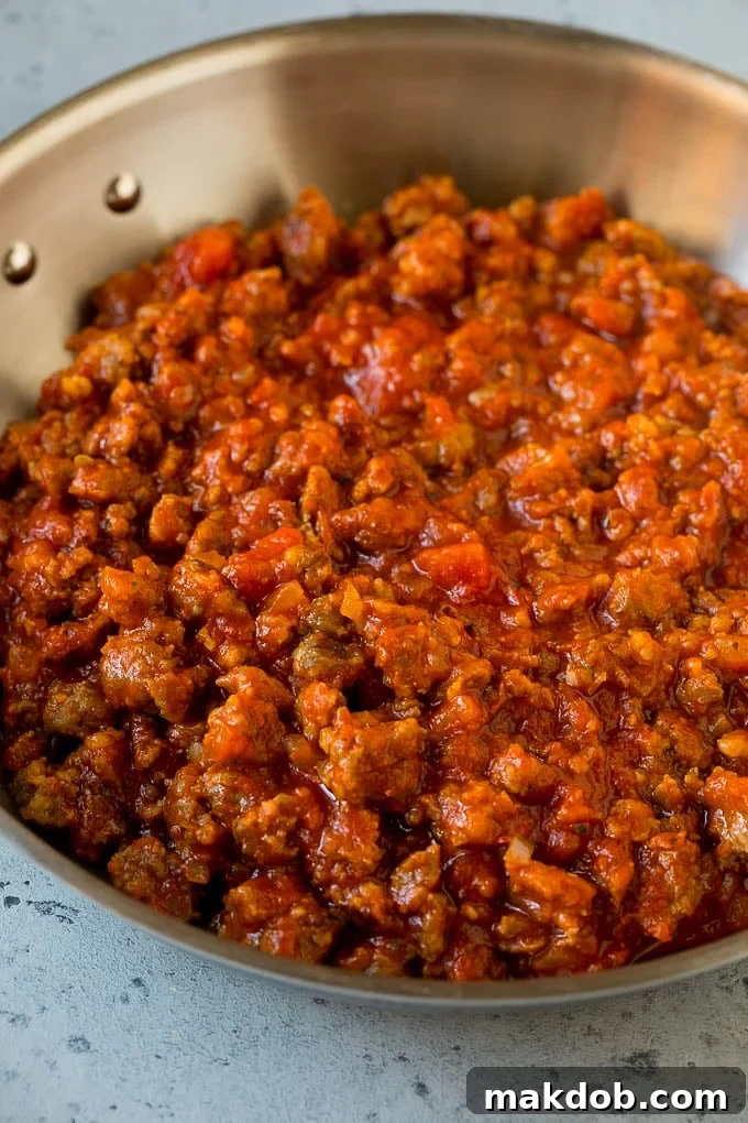 Sausage and tomato sauce simmering in a skillet, creating a rich filling for zucchini boats.