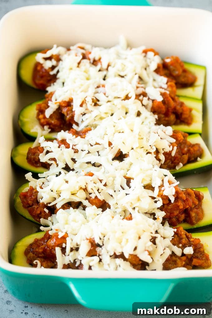 Zucchini boats arranged in a baking dish, filled with a savory meat sauce and topped with shredded cheese, ready for baking.