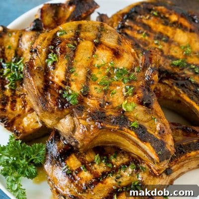Grilled pork chops generously coated with a delicious marinade, served on a platter and garnished with fresh parsley.
