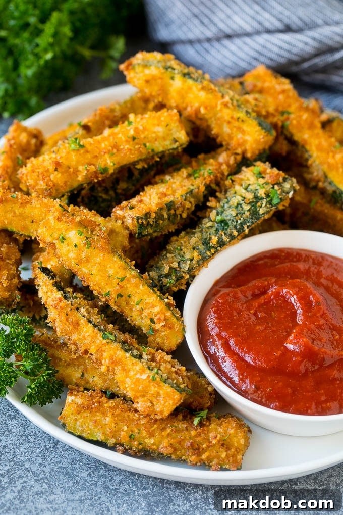 A plate of golden brown fried zucchini sticks served with marinara sauce for dipping, garnished with fresh parsley.