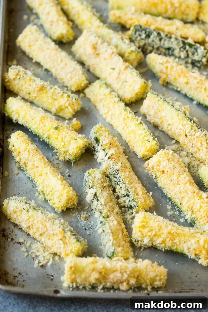 Zucchini sticks coated in a savory mixture of egg, Parmesan cheese, and seasoned breadcrumbs, ready for frying.