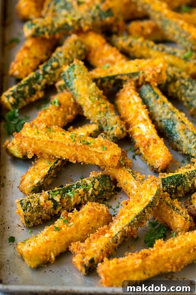 Freshly fried, golden-brown zucchini sticks draining on a sheet pan lined with paper towels.