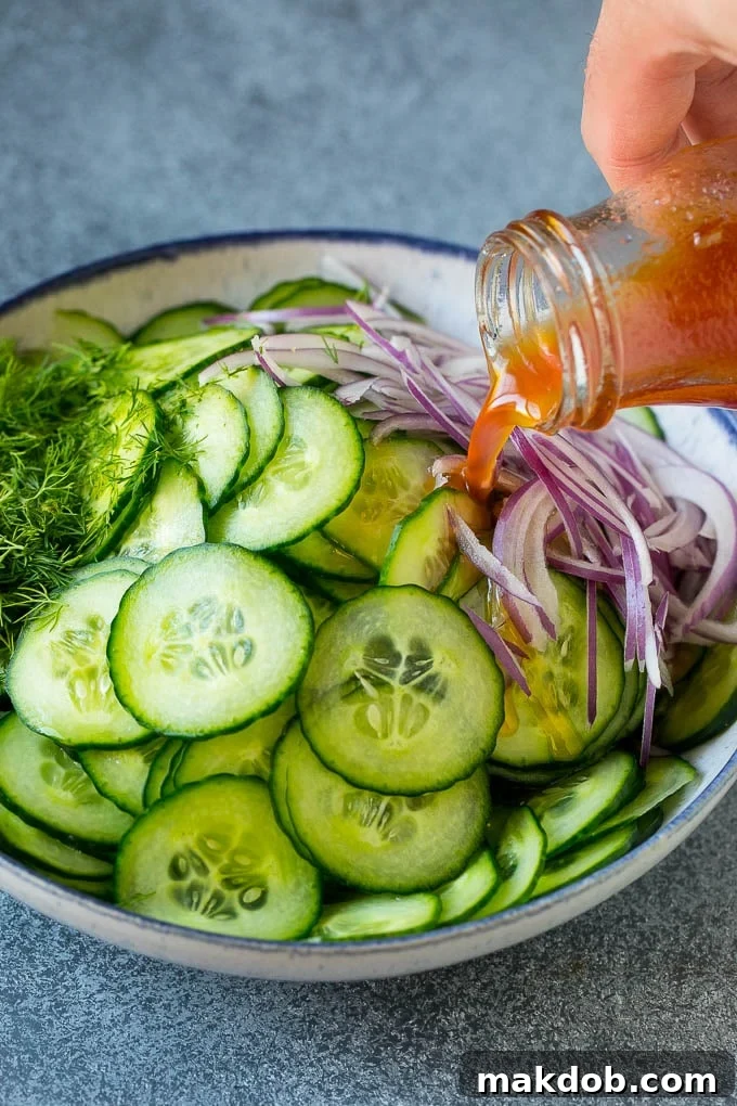 Pouring Dressing Over Cucumber and Dill A hand pouring a vibrant red wine vinaigrette dressing over a bowl of thinly sliced cucumbers and fresh dill.