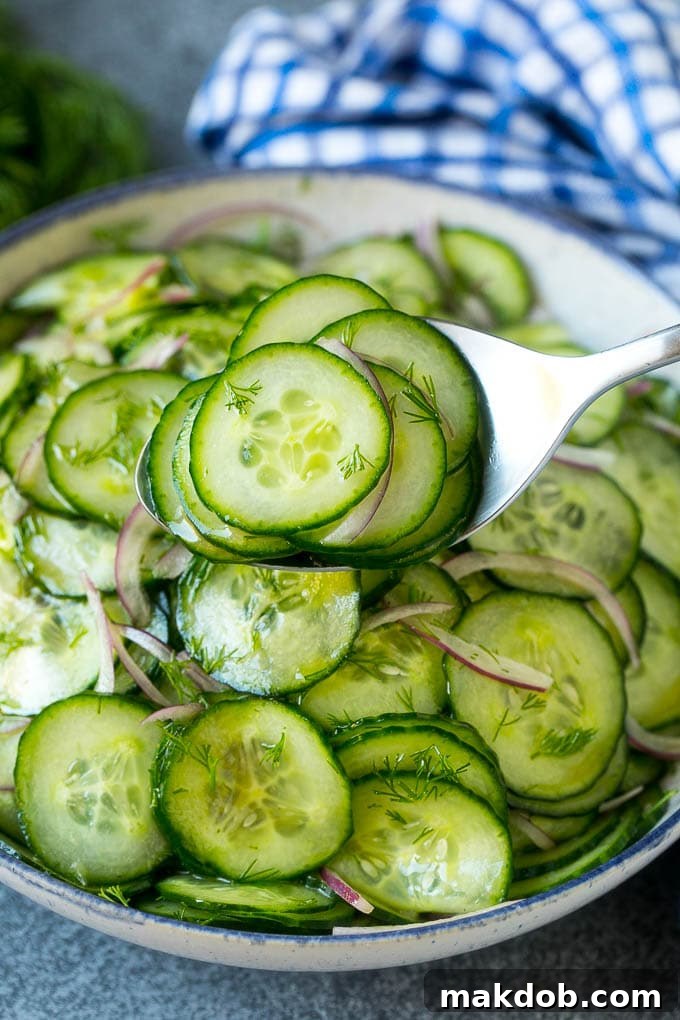 Serving Classic Cucumber Salad A serving spoon lifting a generous portion of classic cucumber salad from a bowl, highlighting the thin slices and fresh dill.
