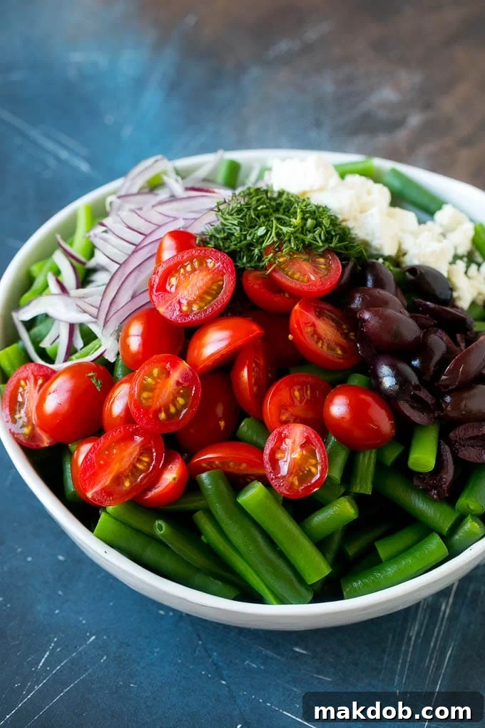 Green Bean Salad Recipe | String Bean Salad | Chopped Salad #greenbeans #tomatoes #olives #salad #cleaneating #lowcarb #glutenfree #dinneratthezoo Vegetables like cherry tomatoes, red onion and olives in a bowl with feta cheese.
