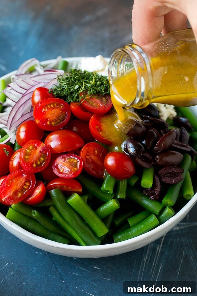 Green Bean Salad Recipe | String Bean Salad | Chopped Salad #greenbeans #tomatoes #olives #salad #cleaneating #lowcarb #glutenfree #dinneratthezoo Dressing being poured over veggies like cherry tomatoes, olives and onions.