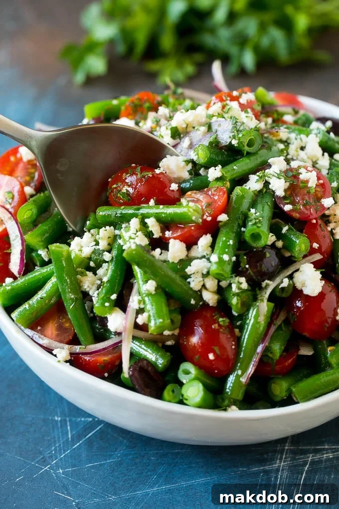 Green Bean Salad Recipe | String Bean Salad | Chopped Salad #greenbeans #tomatoes #olives #salad #cleaneating #lowcarb #glutenfree #dinneratthezoo A serving spoon in a bowl of green bean salad.