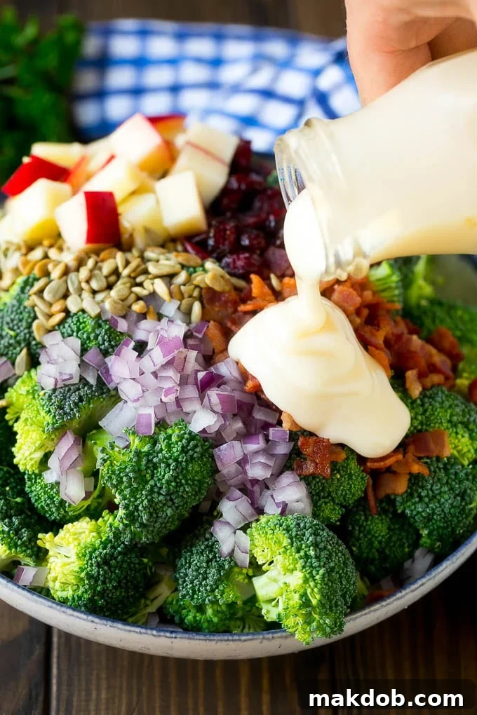 Broccoli Salad Recipe | Creamy Broccoli Salad | Bacon Broccoli Salad #salad #broccoli #bacon #apple #dinneratthezoo #sidedish Creamy dressing being poured over a bowl of broccoli salad ingredients.