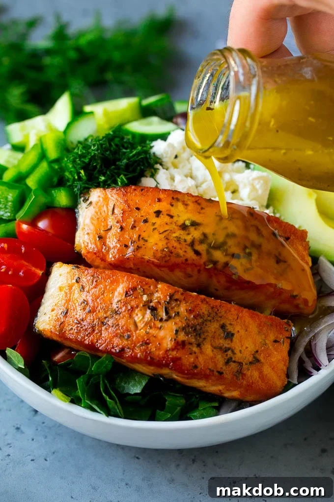 Greek Salmon Salad Recipe | Low Carb Salmon Recipe | Salmon Salad #salmon #seafood #fish #lowcarb #keto #lunch #dinneratthezoo #healthy Salmon fillets on top of greens with dressing being poured over the top.