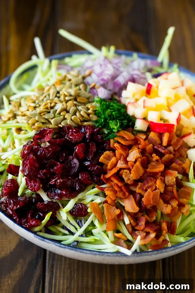 Broccoli slaw, bacon, apples, onion, sunflower seeds and parsley in a bowl.