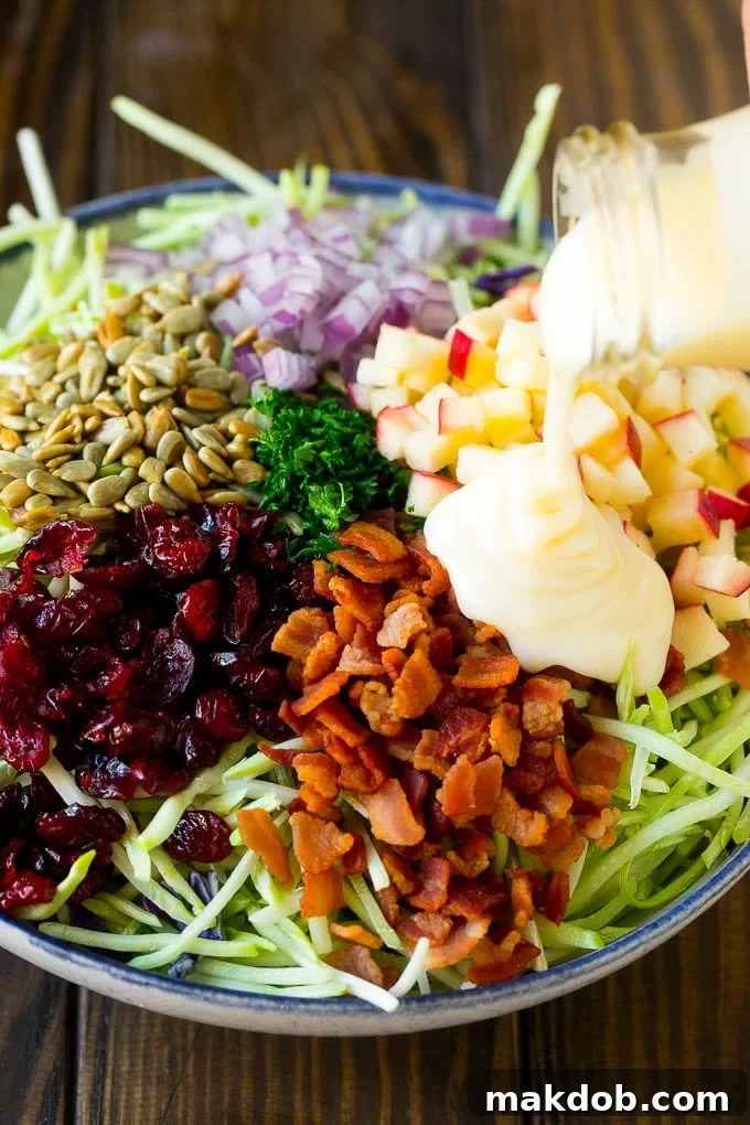 Creamy dressing being poured over broccoli slaw, bacon and apples.