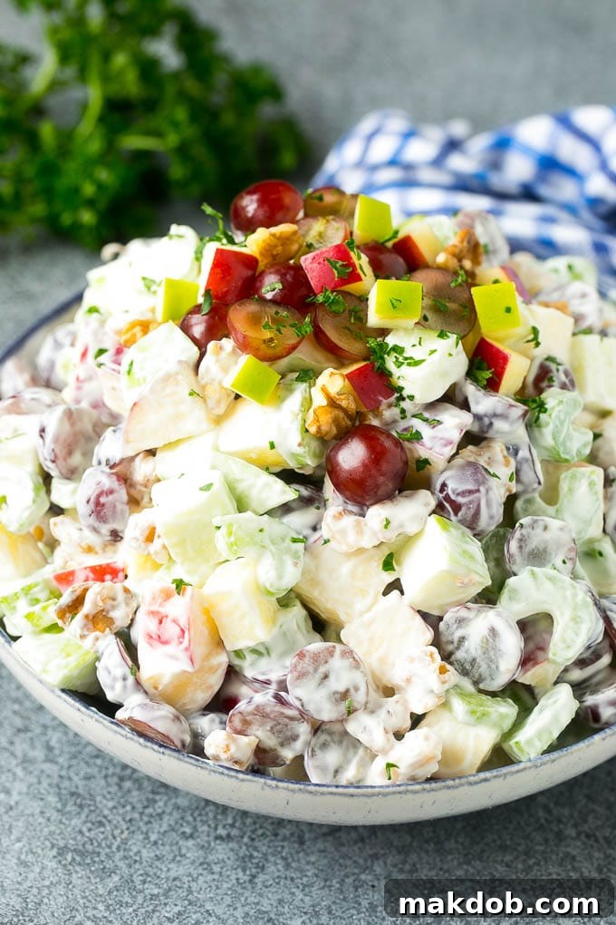 A large bowl of fresh and vibrant Waldorf salad, featuring perfectly diced apples, halved grapes, thinly sliced celery, and chopped walnuts, all generously coated in a rich and creamy dressing, ready for serving.