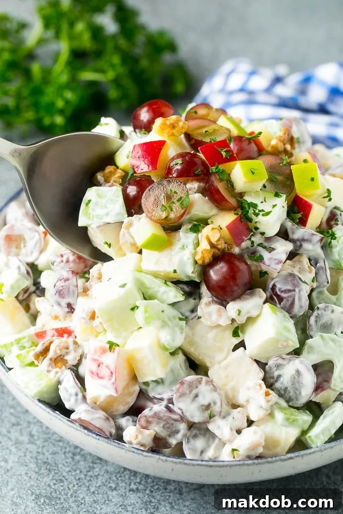 A close-up shot of a serving spoon scooping a portion of a hearty apple walnut Waldorf salad from a rustic wooden bowl, showcasing the creamy dressing coating the fruit, celery, and nuts.