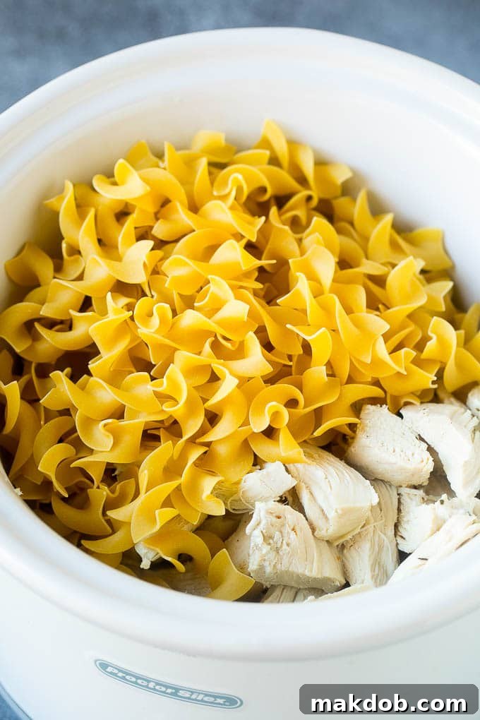 Egg noodles and shredded chicken simmering in a slow cooker filled with golden chicken noodle soup.