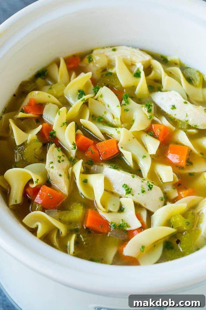 A close-up of slow cooker chicken noodle soup in the pot, showcasing chunky vegetables and chicken.