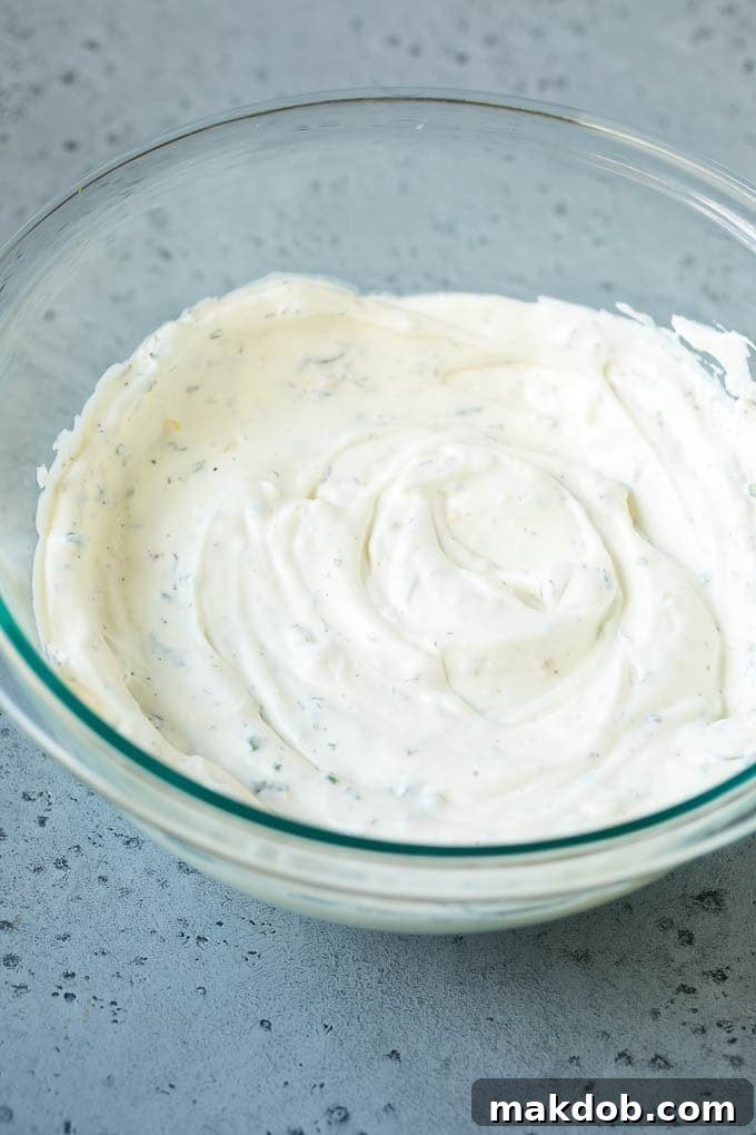 Garden Herb Dip 4 The process of combining ingredients for veggie dip: creamy sour cream and mayonnaise are being mixed together with an array of dried and fresh herbs and savory spices in a bowl, creating a smooth and aromatic base.