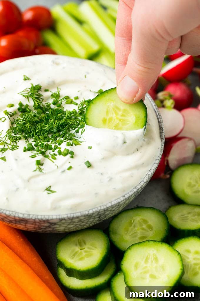 Garden Herb Dip 6 A hand gracefully scoops a generous portion of creamy veggie dip onto a crisp slice of cucumber, highlighting the dip's perfect texture and its ideal pairing with fresh vegetables.